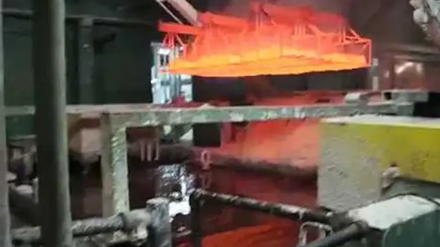 A rack of parts glowing orange as it is lifted over a quench tank, a frame from Upton's own Swing Arm Quenching video